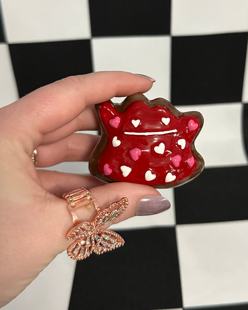 Hand holding a red cat-shaped object with heart patterns on a black and white checkered background