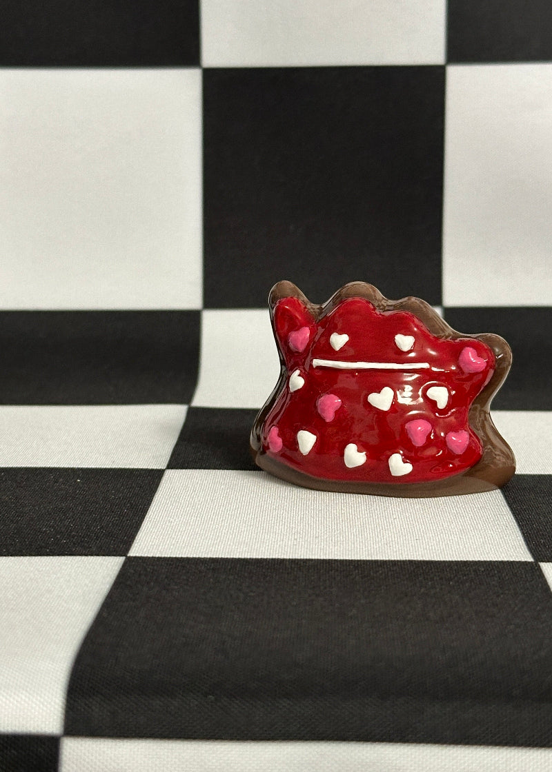 Red heart-shaped cookie with white and pink decorations on a black and white checkered background