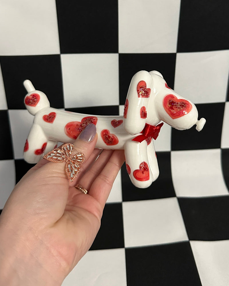 Small dog figurine with red hearts held in front of a black and white checkered background