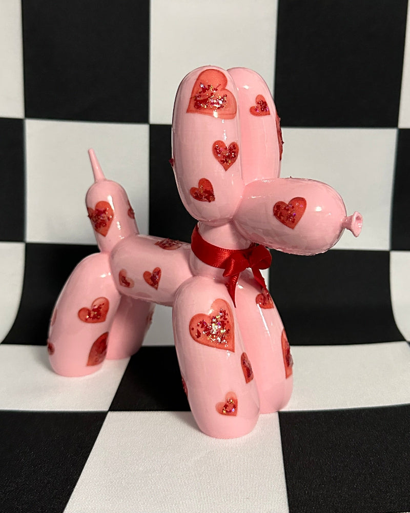 Pink balloon dog figure with heart patterns on a black and white checkered background