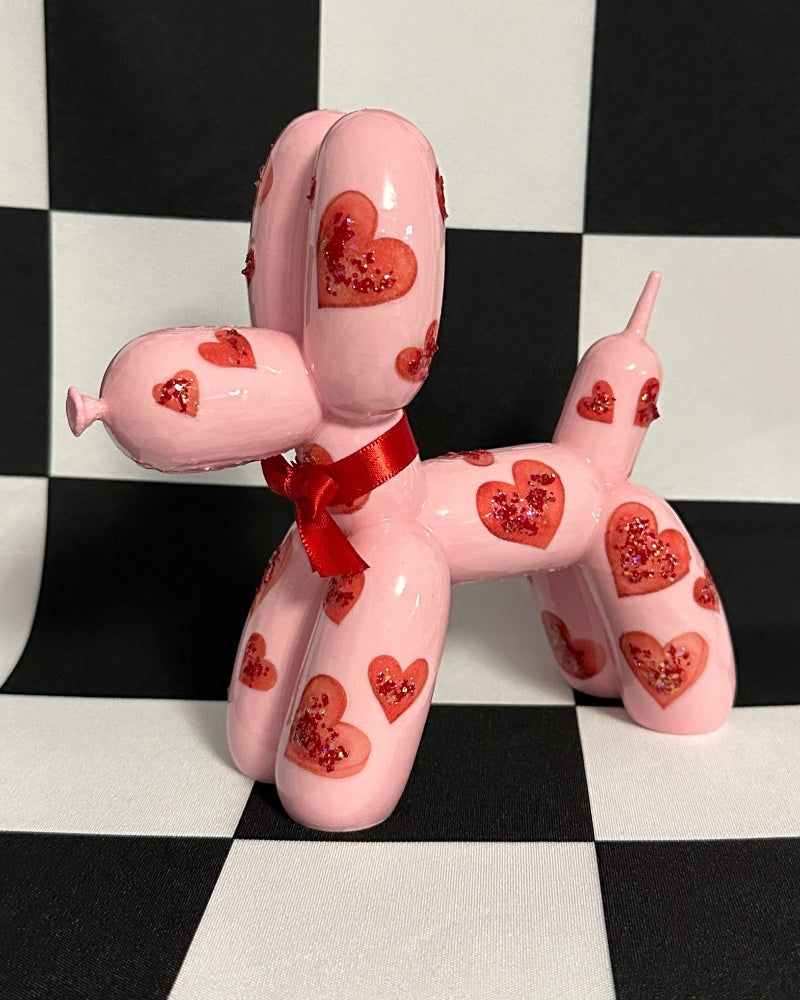 Pink balloon dog figure with heart patterns on a black and white checkered background