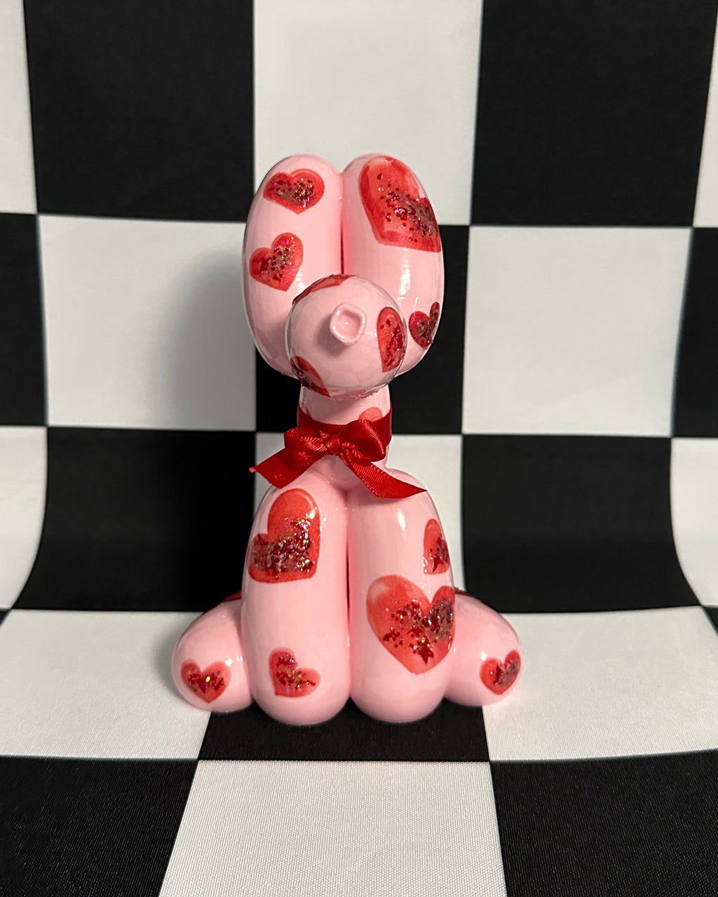 Pink dog figurine with red hearts and a bow tie on a black and white checkered background