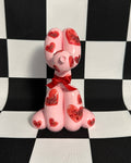 Pink dog figurine with red hearts and a bow tie on a black and white checkered background