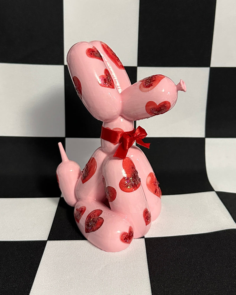 Pink dog toy with red spots and a red bow on a black and white checkered background