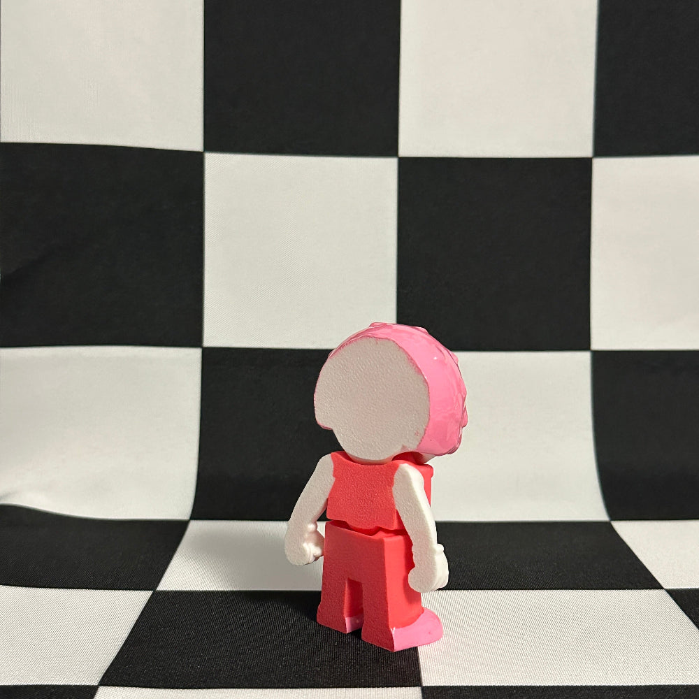Small figurine wearing a pink outfit and helmet on a black and white checkered background