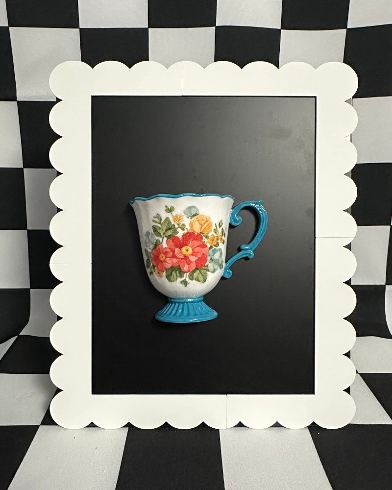 Decorative cup with floral design on a black background, framed by a white scalloped border on a checkered tablecloth.