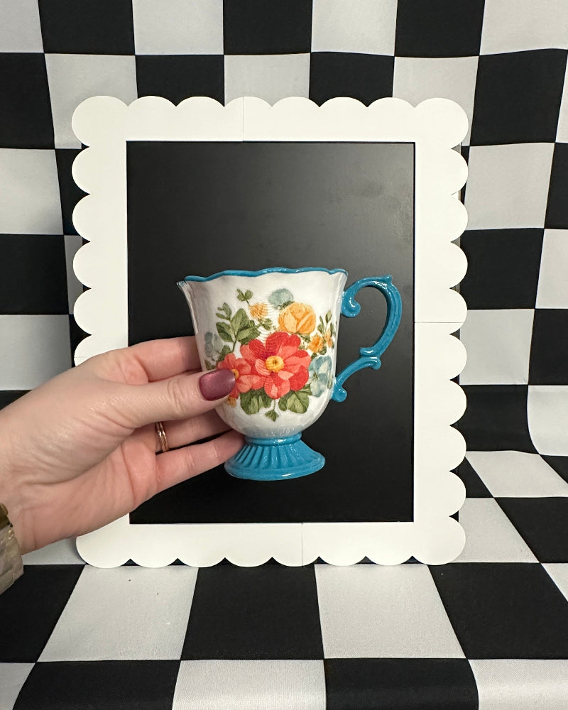 Hand holding a decorative teacup with floral design against a black and white checkered background.