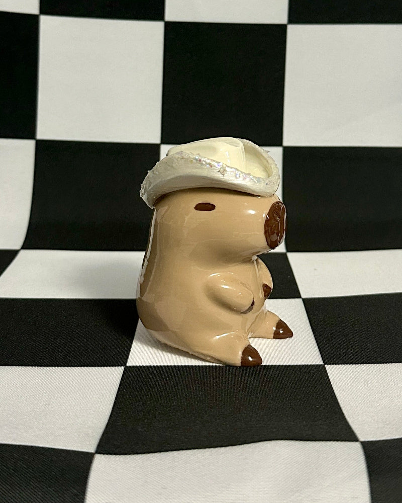 Small figurine of a capybara wearing a hat on a black and white checkered background