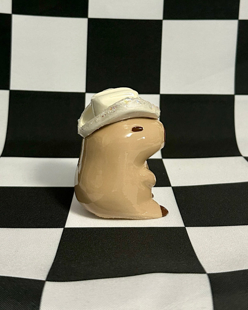 Small ceramic figure wearing a white hat on a black and white checkered background