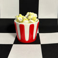 Red and white striped container filled with popcorn on a black and white checkered background