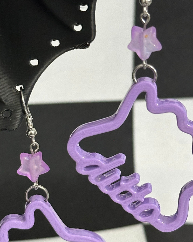 purple ditto earrings hanging from a black cat earring holder on a checkered background