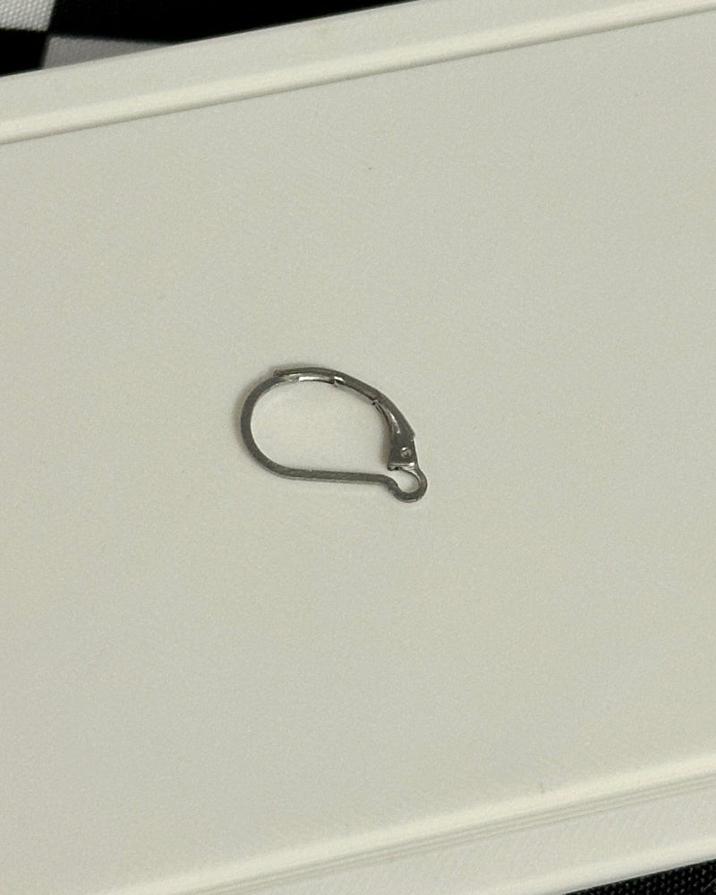 Small metal ring on a white card held by a hand with red and white checkered nail polish against a black and white checkered background.